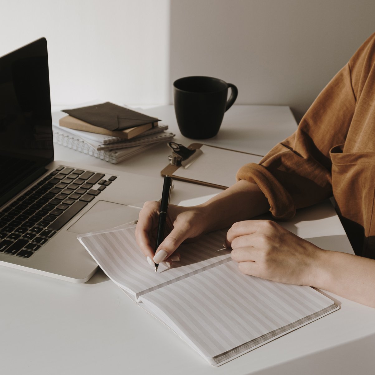 Woman Writing on Notebook near Laptop on the Table